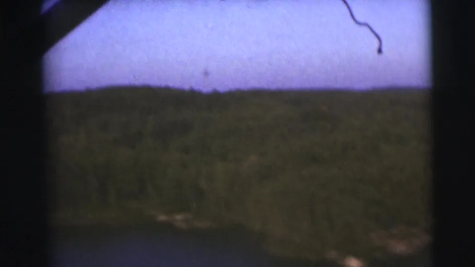 1953 Baraboo, Wisconsin frame showing grassy land near water, a dark wooded horizon, pale sky, and heavy 8mm border shadow.