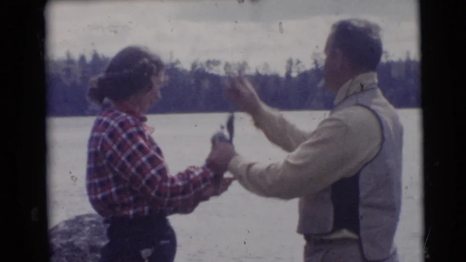 The man lifts fishing line or tackle while the woman stands close by, recorded in soft 8mm color at the Wisconsin lake.