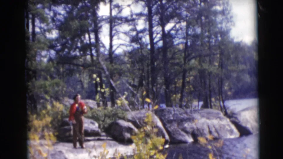 A man stands with a fishing rod on a rocky lakeshore in the Baraboo, Wisconsin 1953 home-movie footage.
