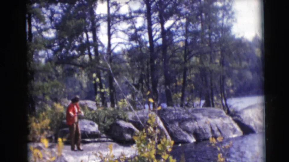 A person in a red jacket appears to check the fishing line on a rocky Baraboo riverbank in 1953 home-movie footage.