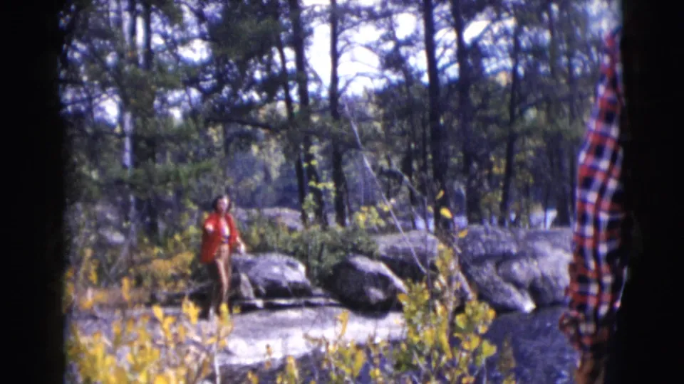 In Baraboo, Wisconsin, a woman in a red coat stands beside grey rocks and trees in 1953 8mm home-movie footage.