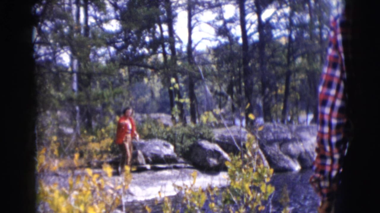 Woman in a red coat stands farther back among rocks and trees.