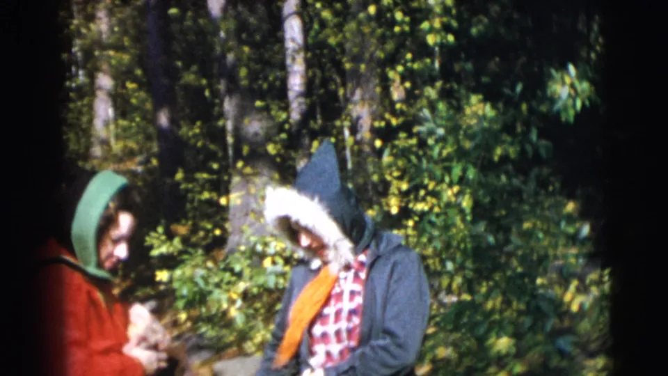 Two women in hooded outerwear stand in the Baraboo woods, one in a red coat and one in a dark fur-trimmed jacket.