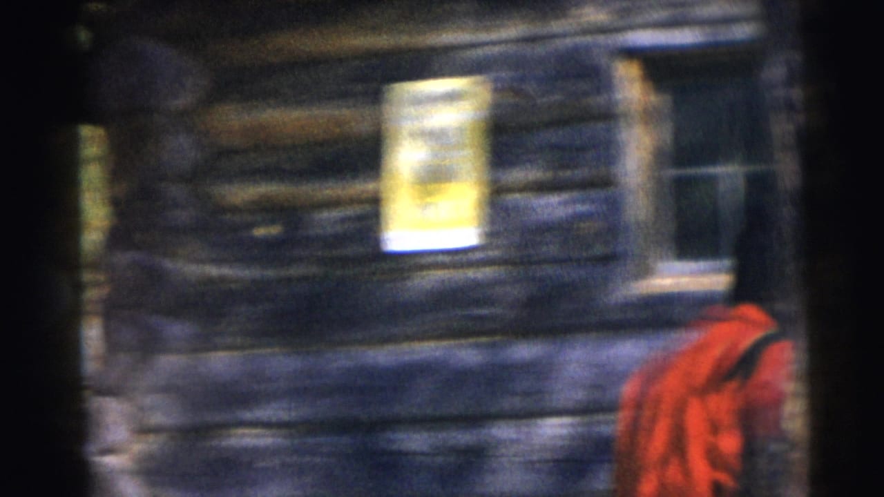 Blurred log cabin wall with a yellow sign and part of a red jacket at the right edge.