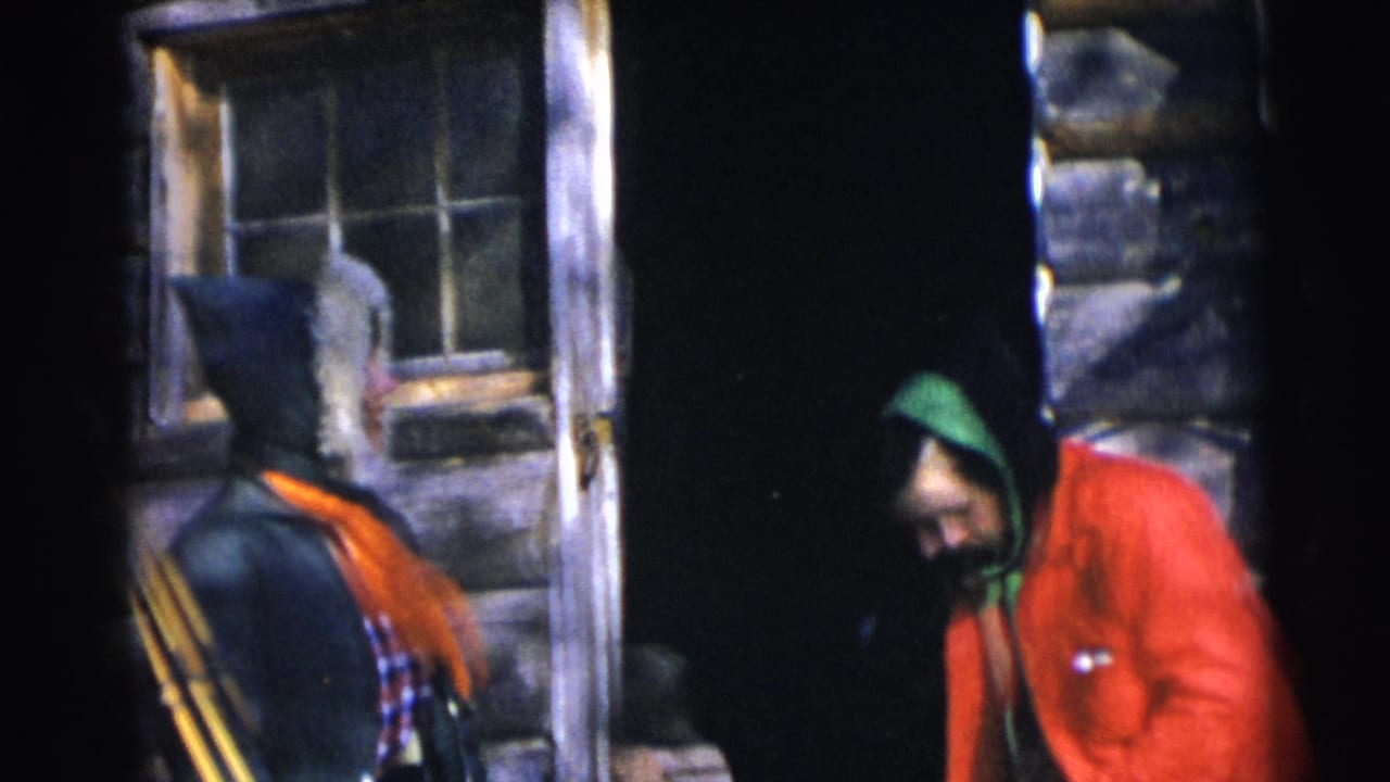 In Baraboo, Wisconsin, 1953 home-movie footage, two adults stand near a log cabin doorway, one in a fur-trimmed hood and orange scarf.