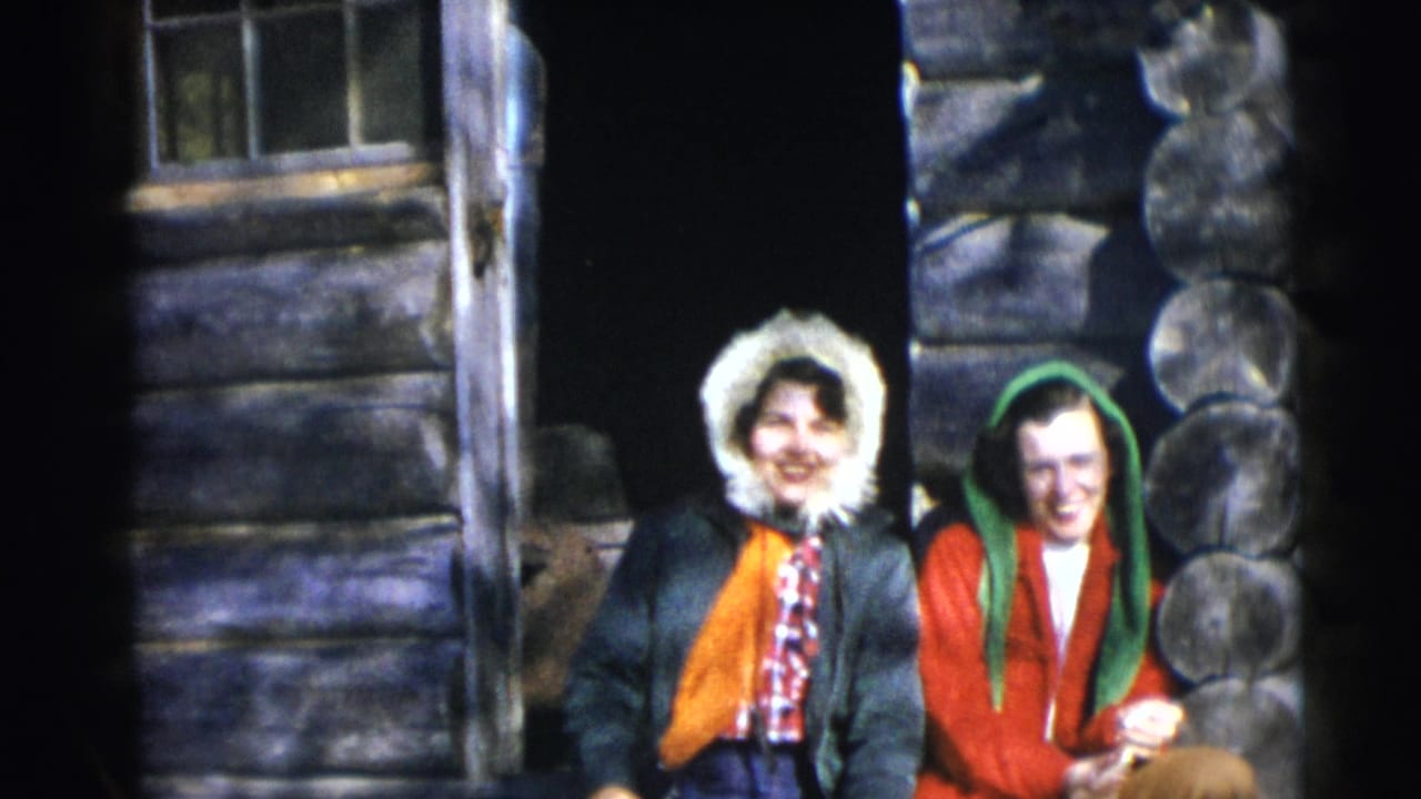 Two young women in winter outerwear smile toward the camera outside a log cabin in Baraboo, Wisconsin, according to the clip metadata.