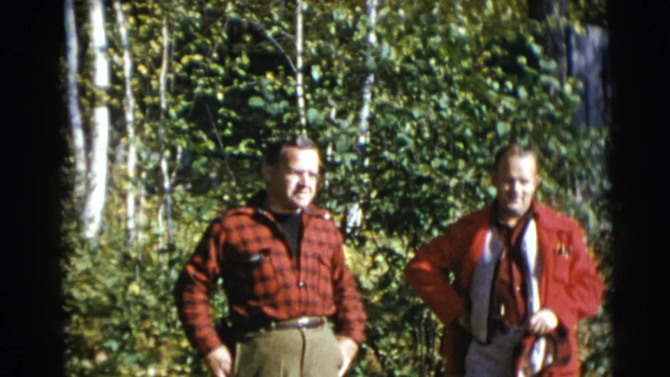 Two men stand in a wooded Baraboo setting, one in a red plaid shirt and one in a red jacket with gear around his neck.