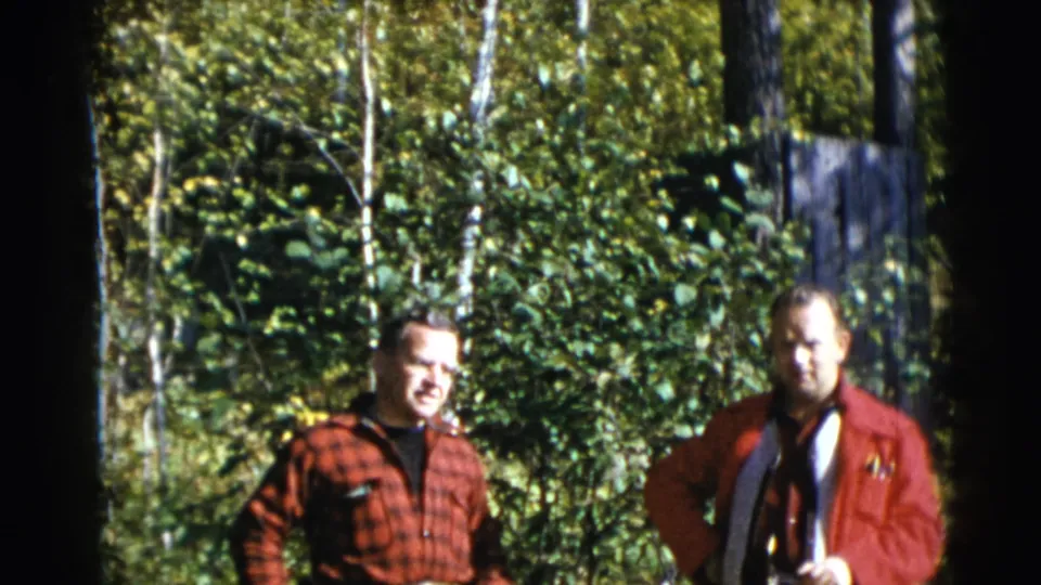 The men remain standing outdoors in 1953 Baraboo footage, framed by birch trunks and sunlit greenery.
