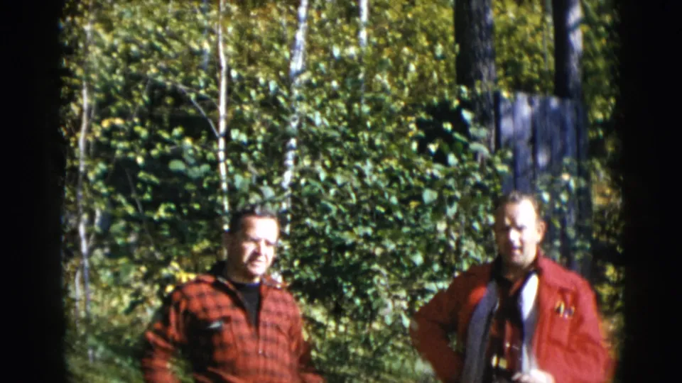 Two adult men in red outerwear stand side by side in a wooded Baraboo setting, captured on 8mm film in 1953.