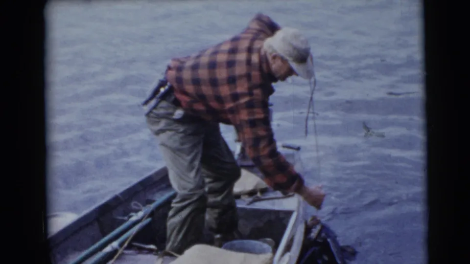 Adult man in plaid shirt and cap leans over a small fishing boat on a lake in Baraboo, Wisconsin footage from 1953.