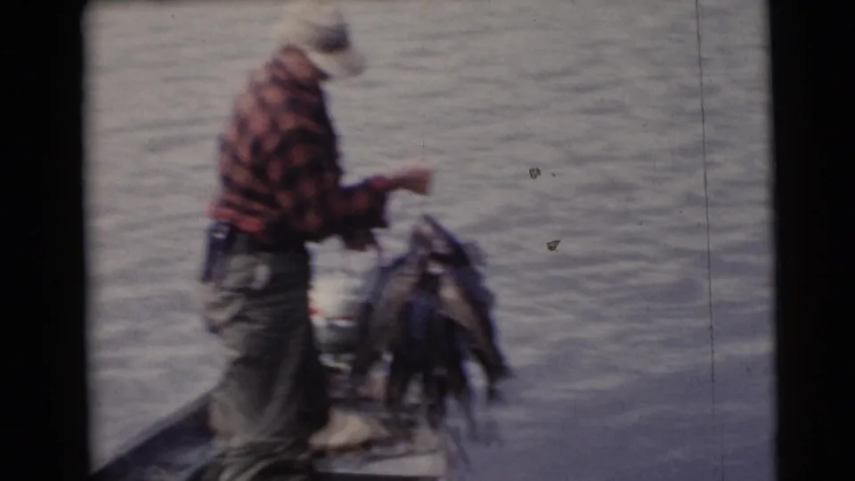 A man in red plaid stands near the boat edge with a visible stringer of fish during the Wisconsin fishing trip.