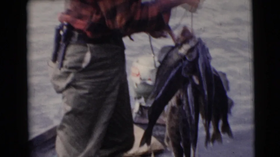 Close framing shows the man in red plaid next to a hanging stringer of fish, with water behind him.
