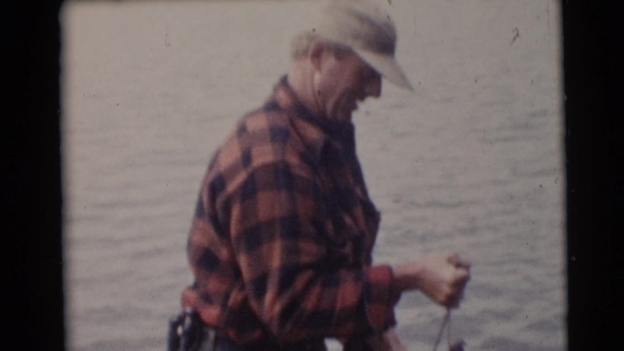 An adult angler in a red plaid shirt and light cap stands on a small boat in the Baraboo, Wisconsin fishing footage.