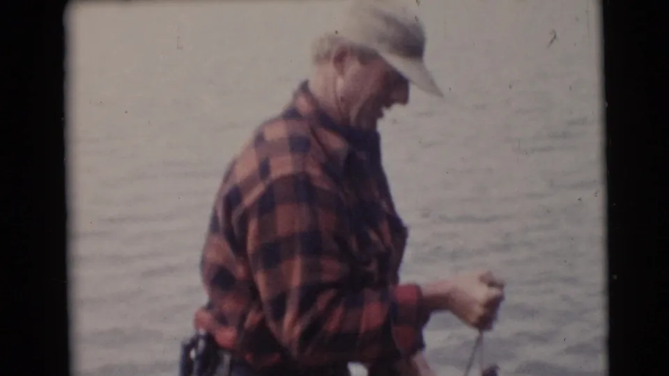 An adult angler in a red plaid shirt and light cap stands on a small boat in the Baraboo, Wisconsin fishing footage.