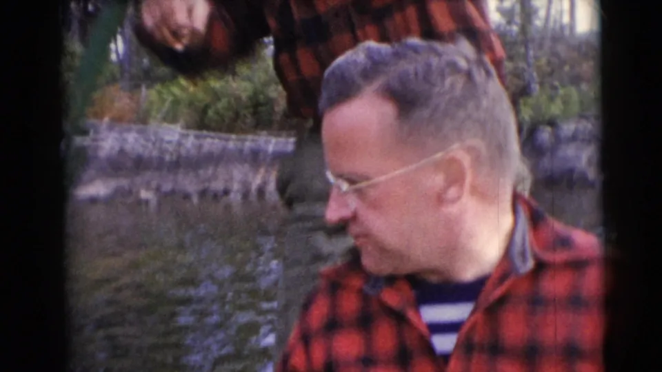Two adult men in red shirts appear near the water and shoreline in the 1953 Baraboo, Wisconsin fishing home movie.