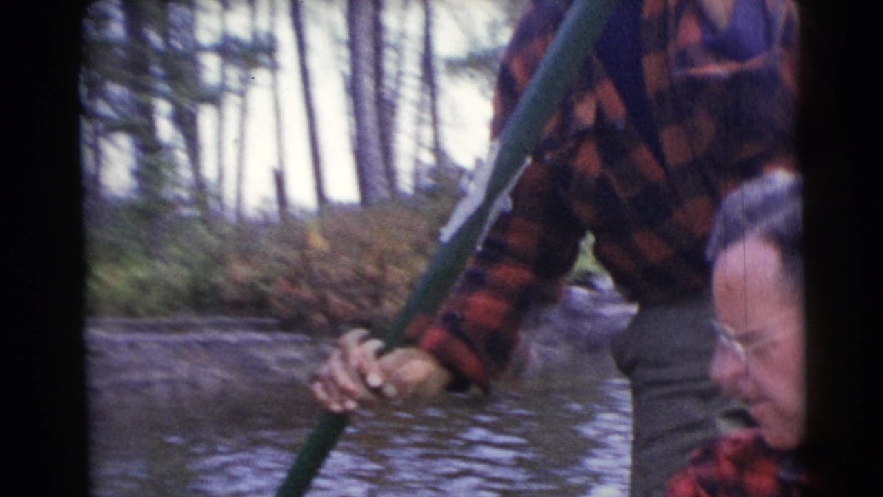 In the 1953 Baraboo 8mm footage, one man stands with a green pole as another sits near the side of the boat.