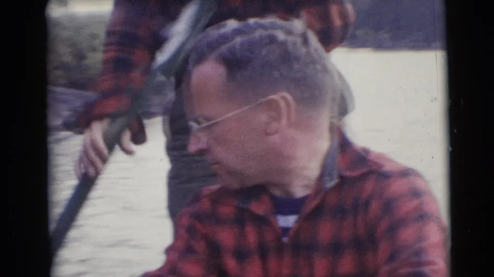 A seated man in glasses appears in a small boat in Baraboo, Wisconsin, with another man standing behind him in 1953 footage.