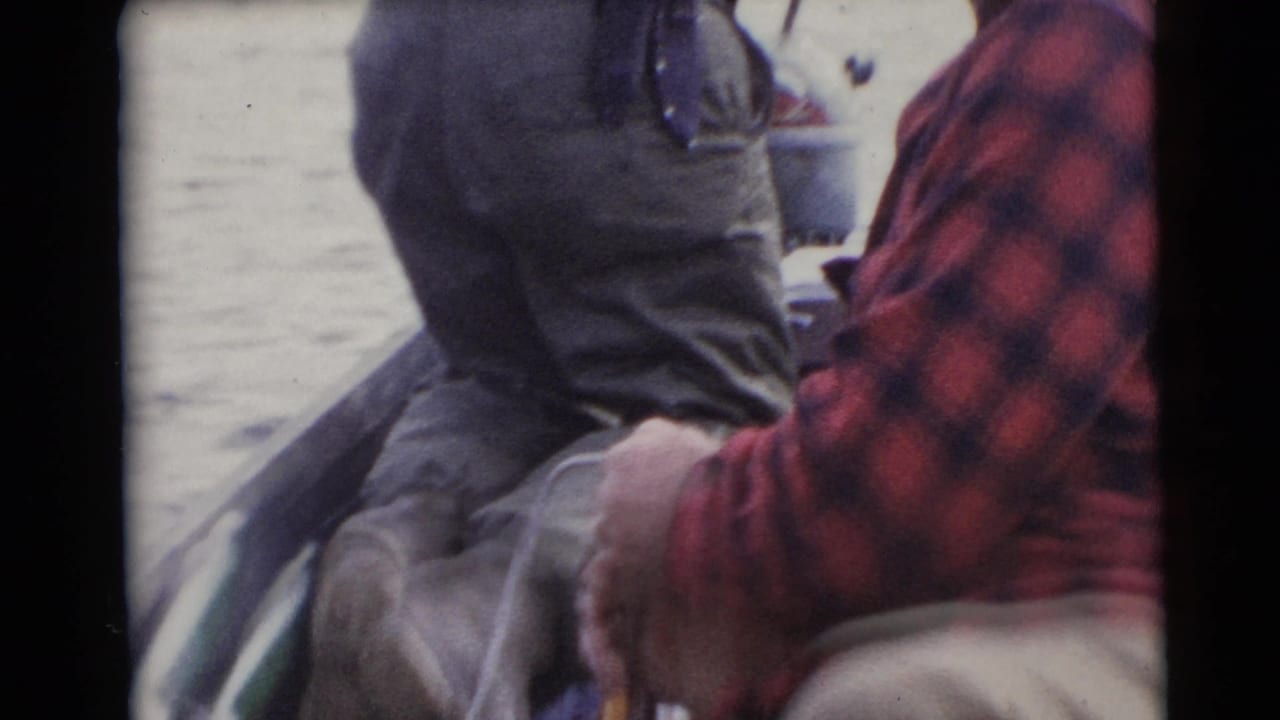 1953 Baraboo, Wisconsin home-movie frame of two adult men in plaid shirts seated in a small boat on the water.