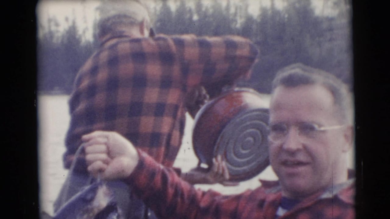 In 1953 Baraboo, Wisconsin home-movie footage, a man in a red plaid shirt displays a large fish beside a canoe on a lake or river.