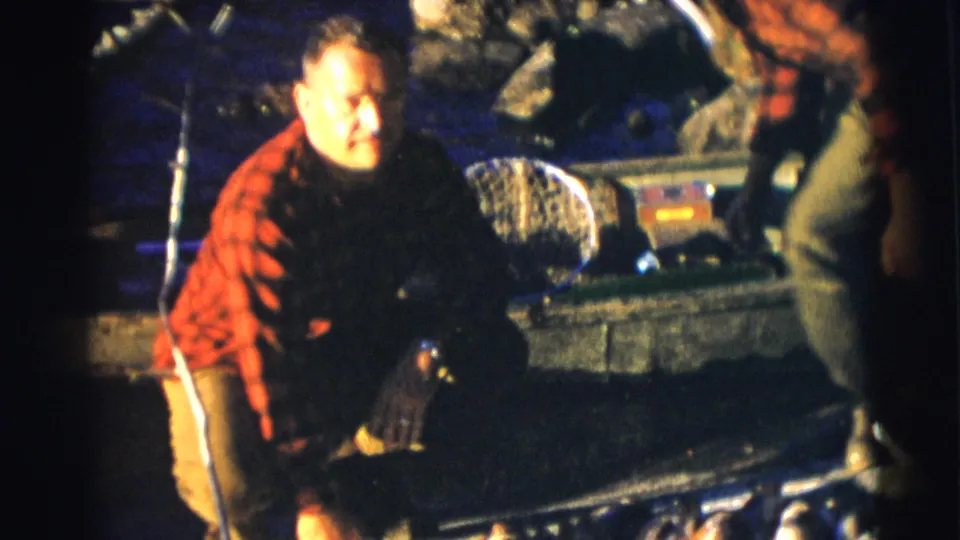 A man in a red plaid shirt kneels by the boat, with fishing gear and the catch nearby in Baraboo, Wisconsin.