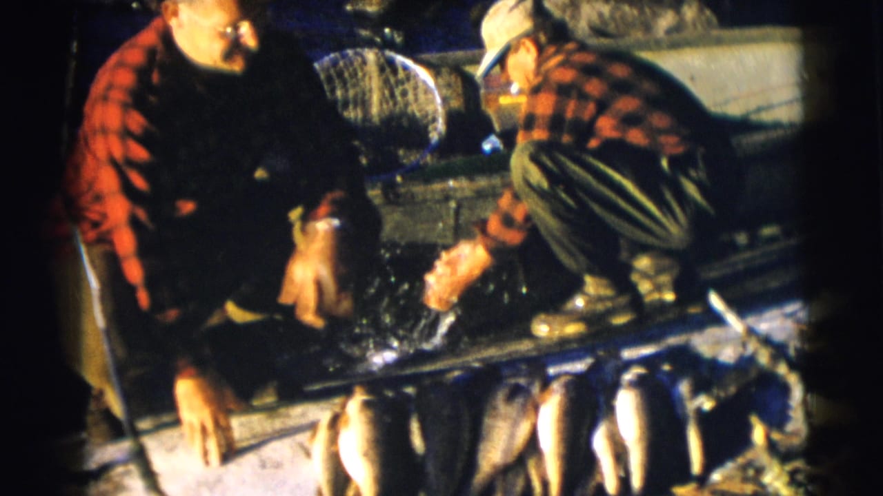 Two men crouch in a boat beside a row of freshly caught fish.