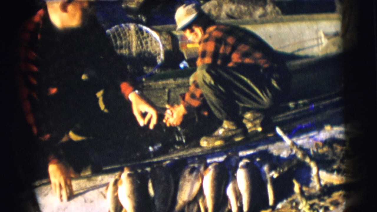 1953 Baraboo, Wisconsin fishing footage with two men crouched in a boat and several fish visible along the foreground.