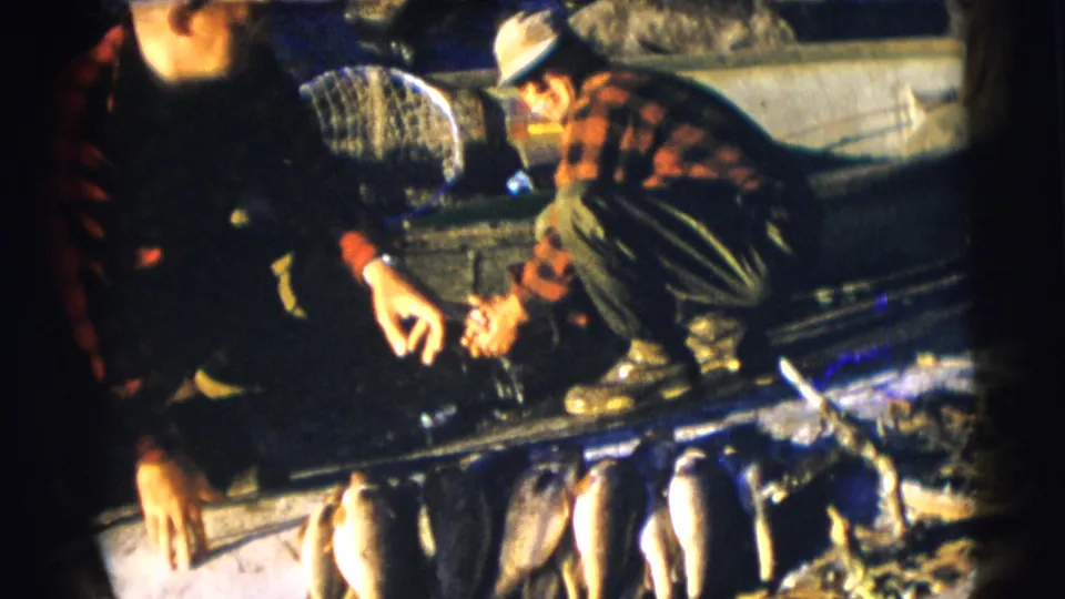 1953 Baraboo, Wisconsin fishing footage with two men crouched in a boat and several fish visible along the foreground.