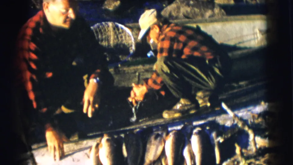 1953 8mm home-movie frame from Baraboo, Wisconsin showing two adults working around a fresh fish catch in a boat.