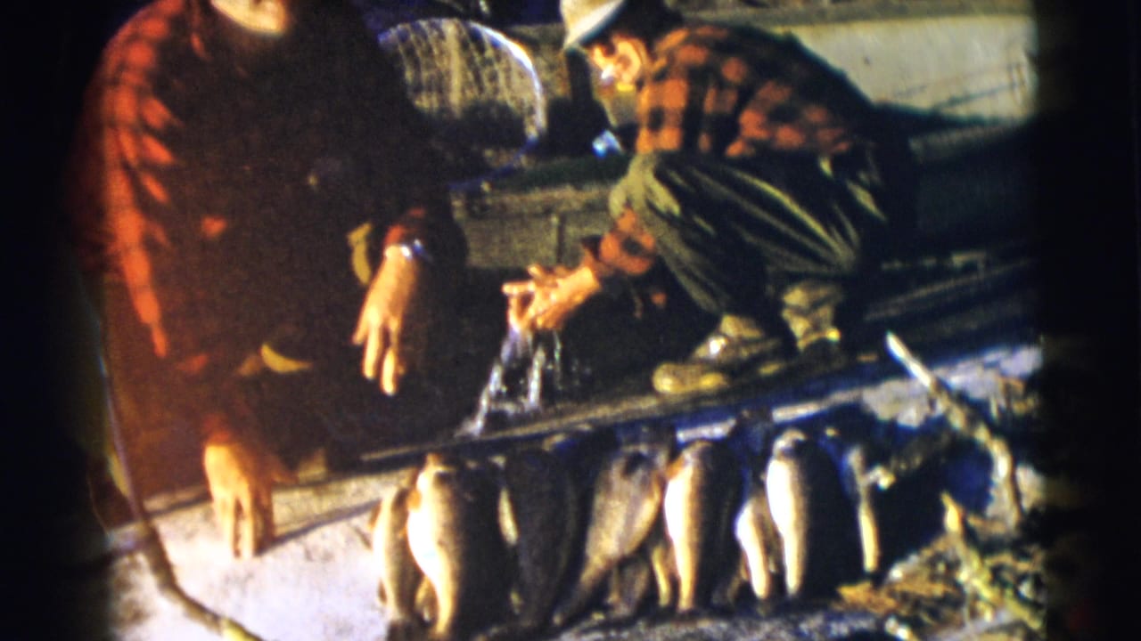 In Baraboo, Wisconsin, 1953 home-movie footage, two adult men in red plaid shirts crouch beside a boat with a row of fish on display.