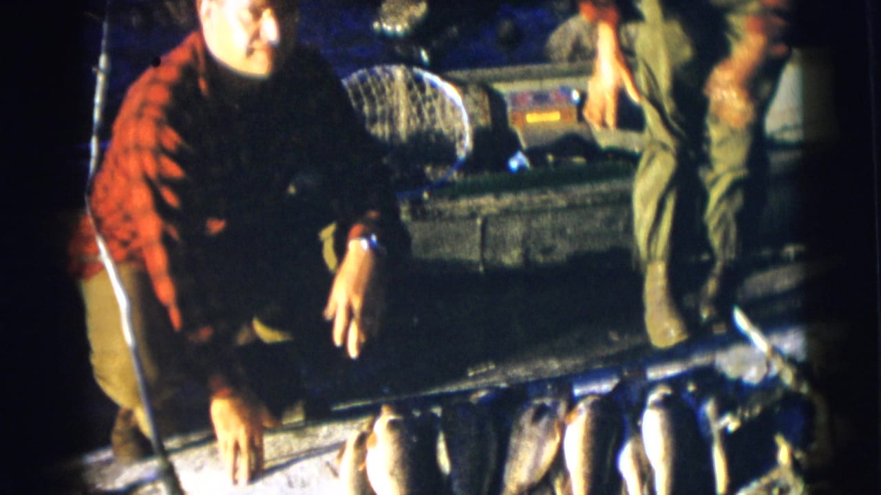 Man crouching by a boat while another person stands near fish on the deck.