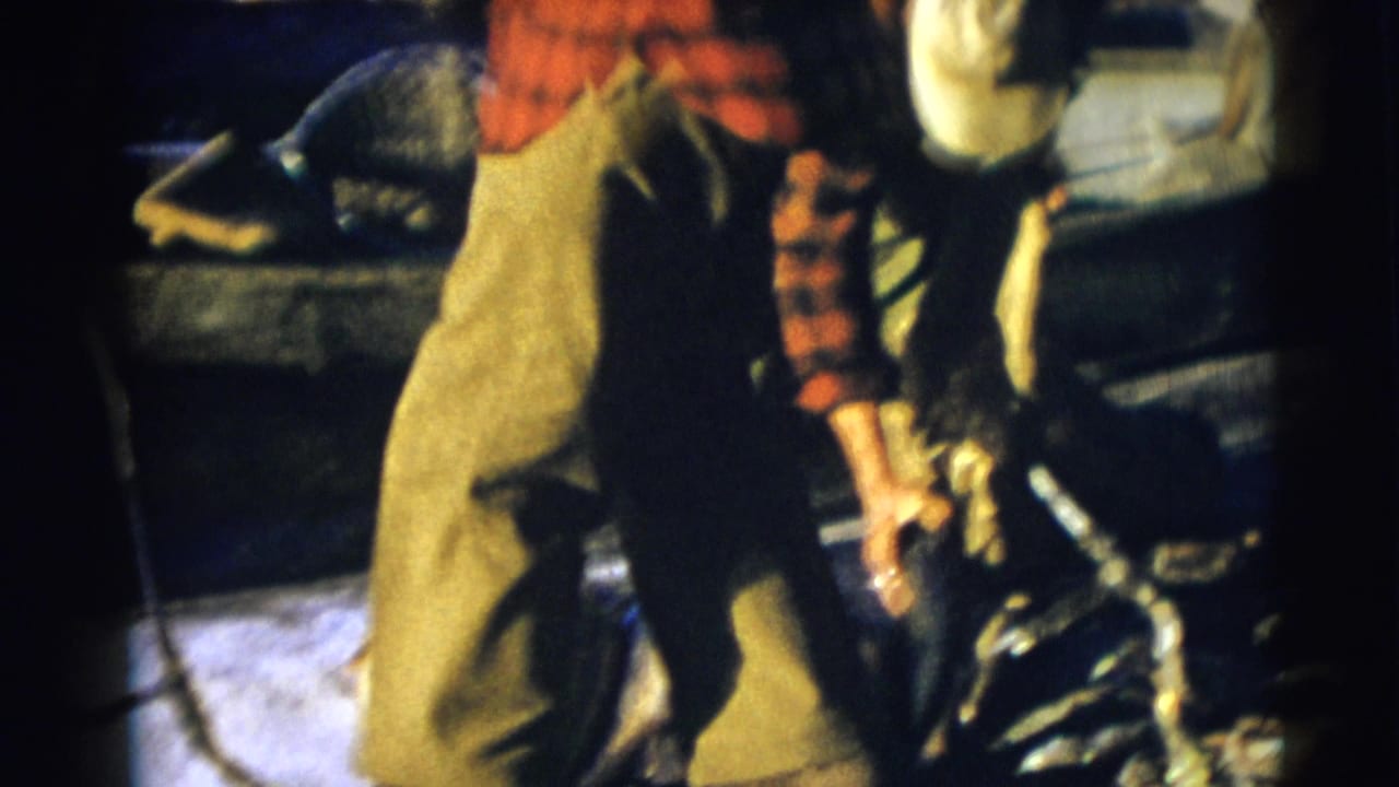 1953 Baraboo, Wisconsin frame with a plaid-shirted fisherman near the boat, holding or standing beside a large fish in low light.