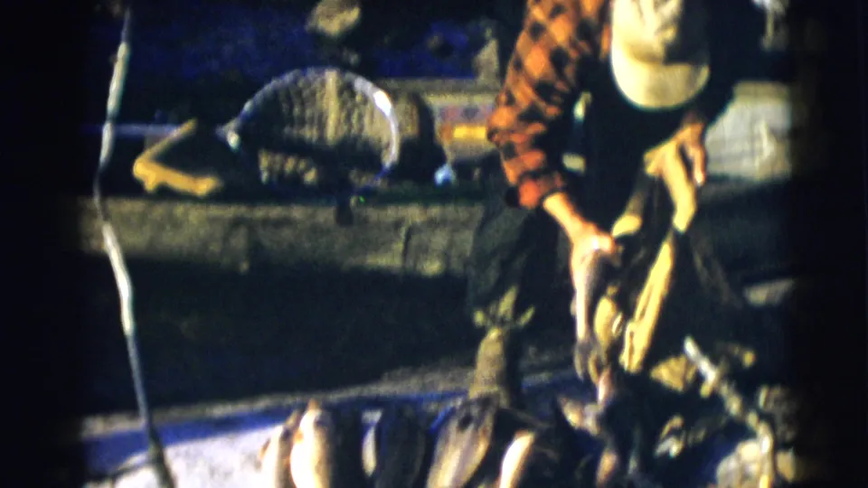 1953 Baraboo, Wisconsin 8mm still of a man in plaid bending over fish and gear beside a boat at night.