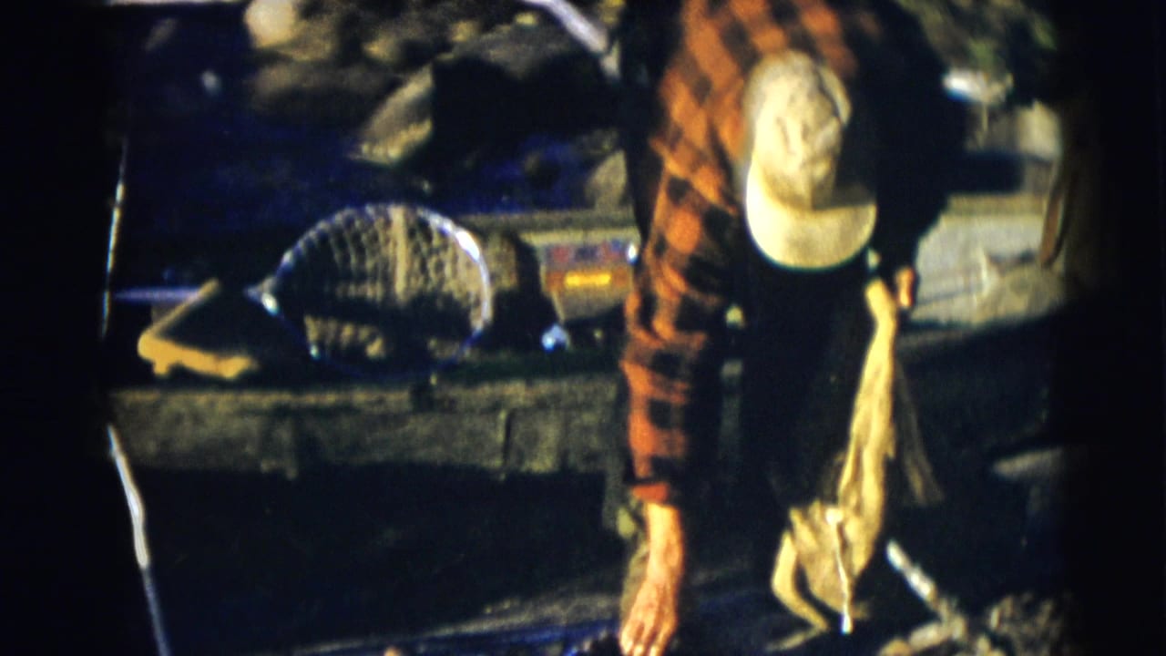 Fisherman in a red plaid shirt bends over a boat with a landing net nearby.