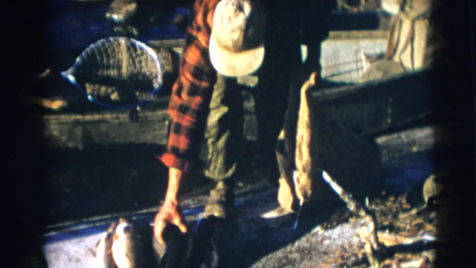 The Baraboo fisherman, filmed in 1953 on 8mm, reaches toward fish in the boat while a sack and net remain visible nearby.