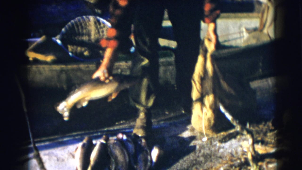Man holds a fish over the side of a boat near a burlap sack and net.