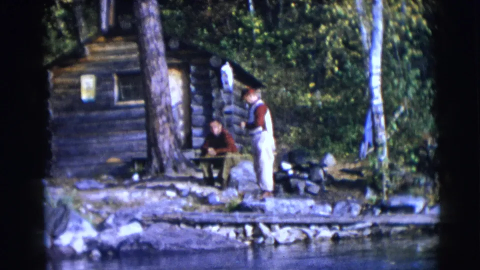 Two people appear near a lakeside log cabin in the Baraboo, Wisconsin footage, with trees, water, and shore gear visible.