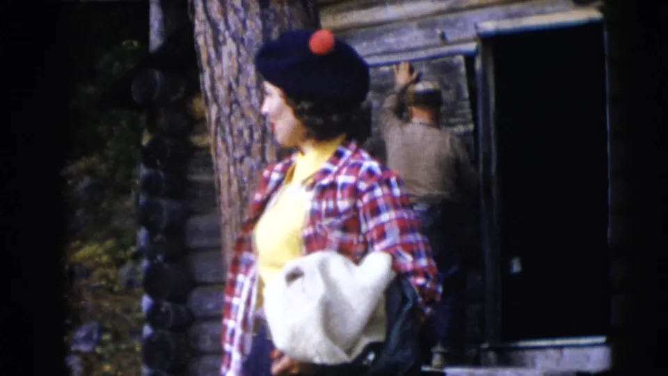 Near Baraboo in 1953, the woman in plaid stands by a log cabin while another adult is seen entering the dark doorway.