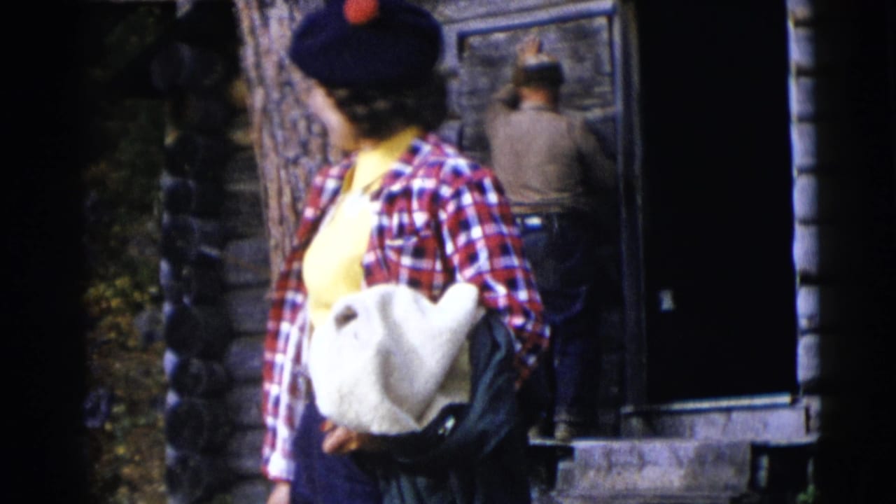 In 1953 Baraboo, Wisconsin footage, a woman in plaid and a navy beret stands near a log cabin while adults work by the door.