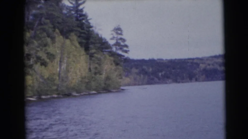 1953 Baraboo, Wisconsin home-movie frame showing open river water, a receding forested shoreline, and distant wooded hills.