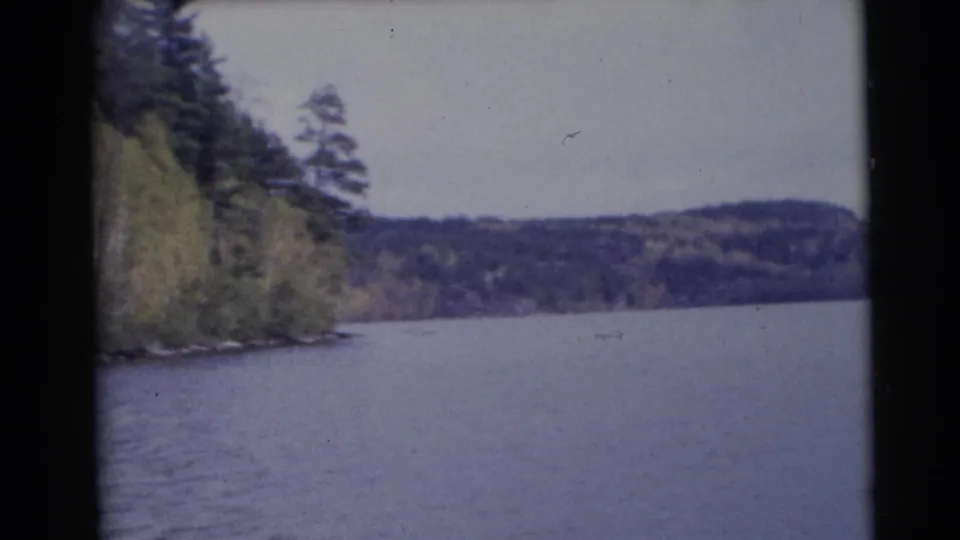 1953 Baraboo, Wisconsin 8mm frame with broad river water, a narrow wooded bank at left, distant hills, and faded color.