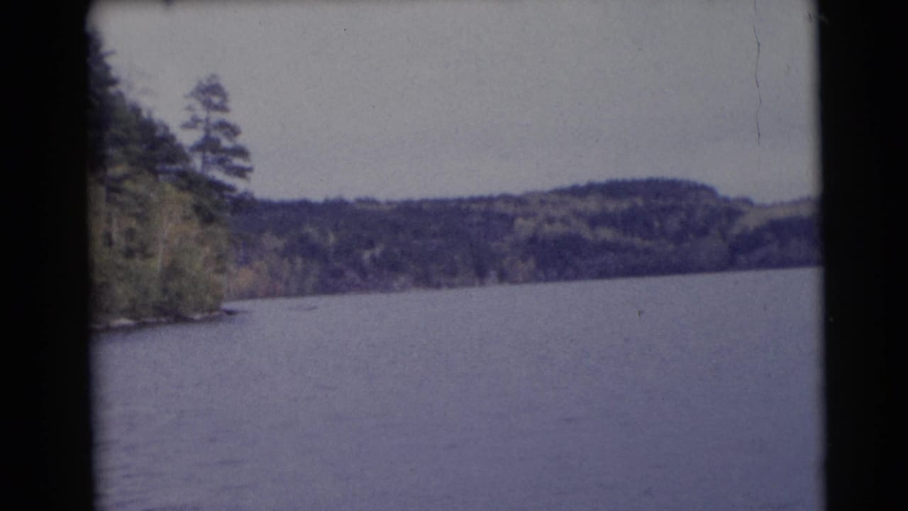 Calm lake with wooded hills and a tree-lined left shore under an overcast sky.