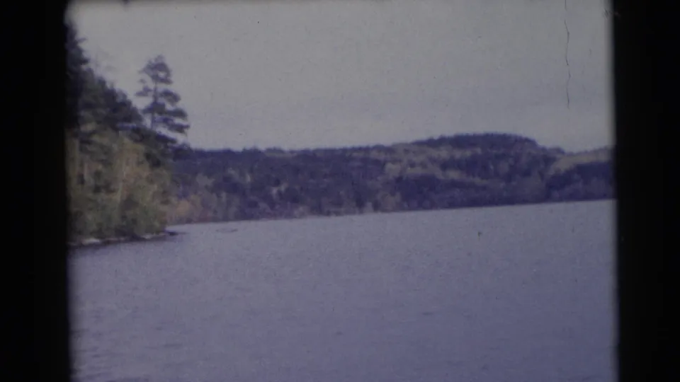 1953 Baraboo, Wisconsin 8mm frame showing a calm lake, distant wooded hills, and trees along the left shoreline.