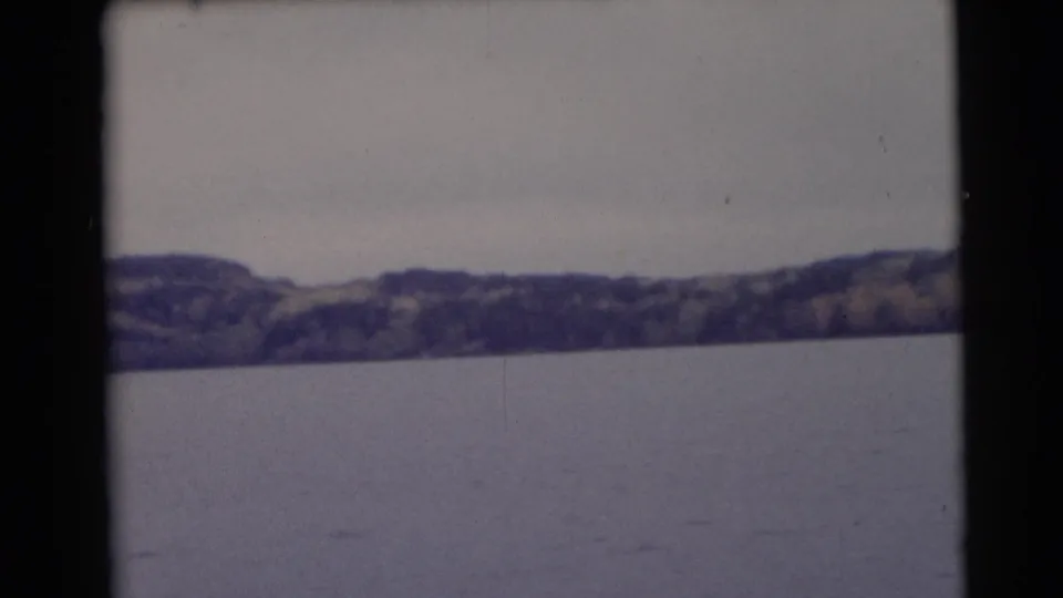 1953 Baraboo, Wisconsin scenic frame with calm lake water, forested hills, overcast sky, and visible 8mm borders.