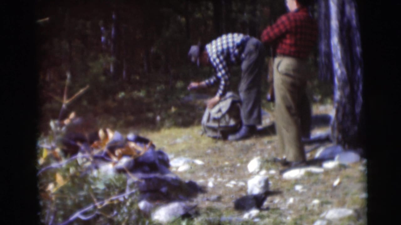 Two adult men in a Baraboo, Wisconsin wooded clearing in 1953, one bending toward a backpack while the other stands nearby.
