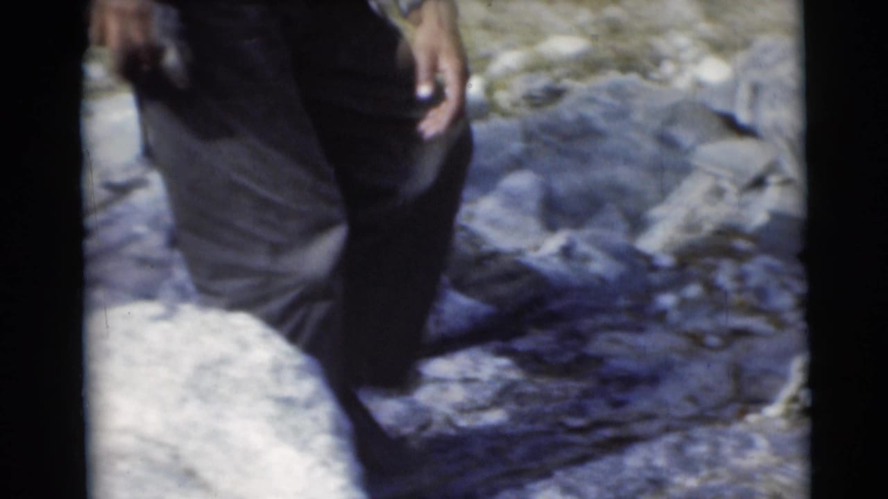 A man’s legs and hand pass through a rocky woodland area in the 1953 Baraboo camping home movie.