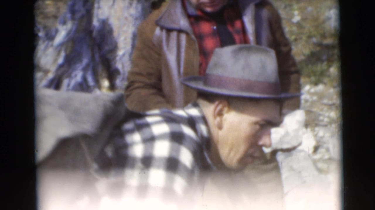 In 1953 Baraboo, Wisconsin home-movie footage, two adult men stand near shore as one in a fedora leans toward the water.