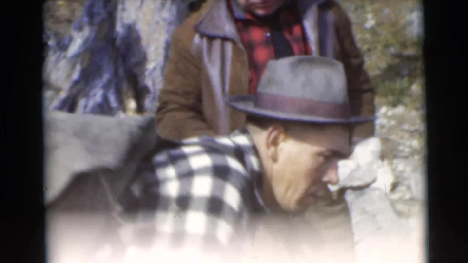In 1953 Baraboo, Wisconsin home-movie footage, two adult men stand near shore as one in a fedora leans toward the water.