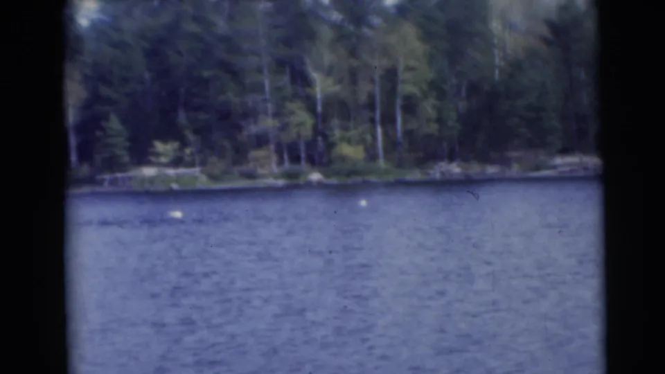 A wide Baraboo, Wisconsin lakeside shot shows rippled water, a wooded shore, and small light specks on the lake surface.