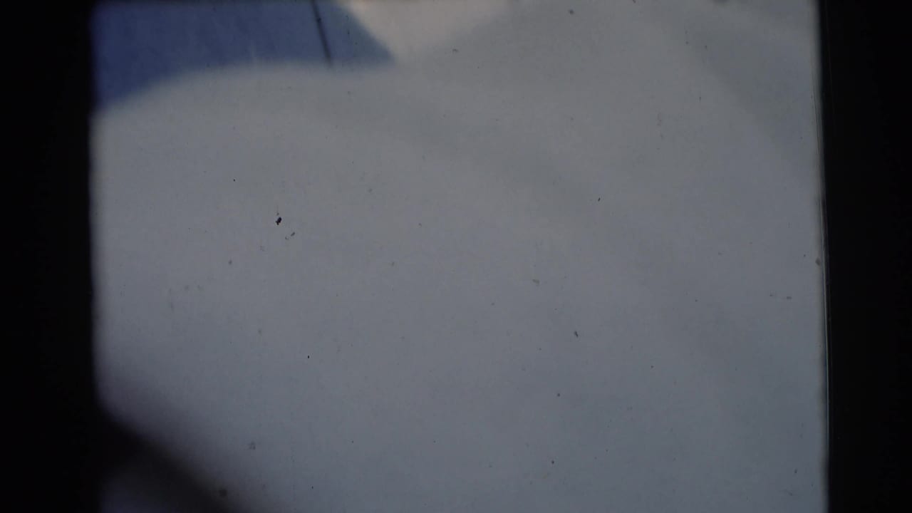 Pale blanket surface fills the frame with a dark vertical film edge and faint dust specks.