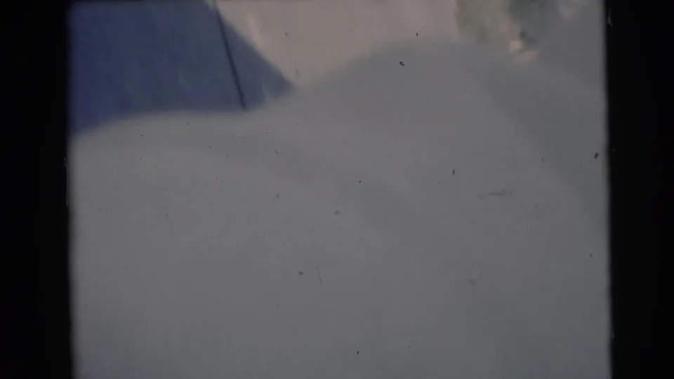 Soft 8mm frame from Baraboo showing pale bedding or a light blanket with blue-gray shadow and visible film wear.